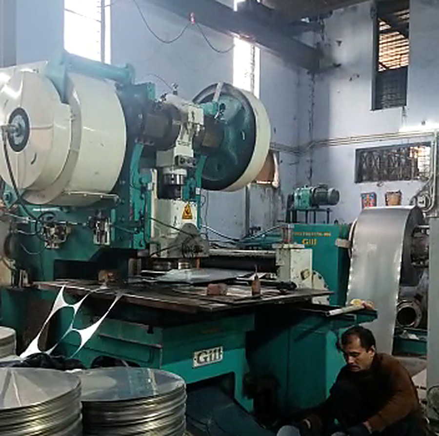Stacks of blanked stainless steel circles beside the press