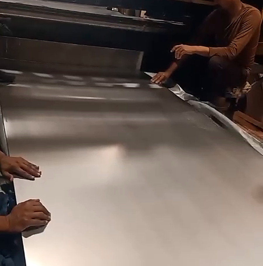 Two operators drawing out a finished stainless steel sheet to check the surface